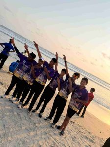 Six young cricket players from MP Tiger wearing purple Goa Heroes Cup jerseys posing and gesturing victory signs at sunset on the beach.